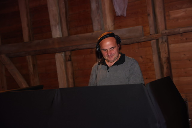 Professional DJ wearing headphones and mixing music at an event with a rustic wooden wall background.