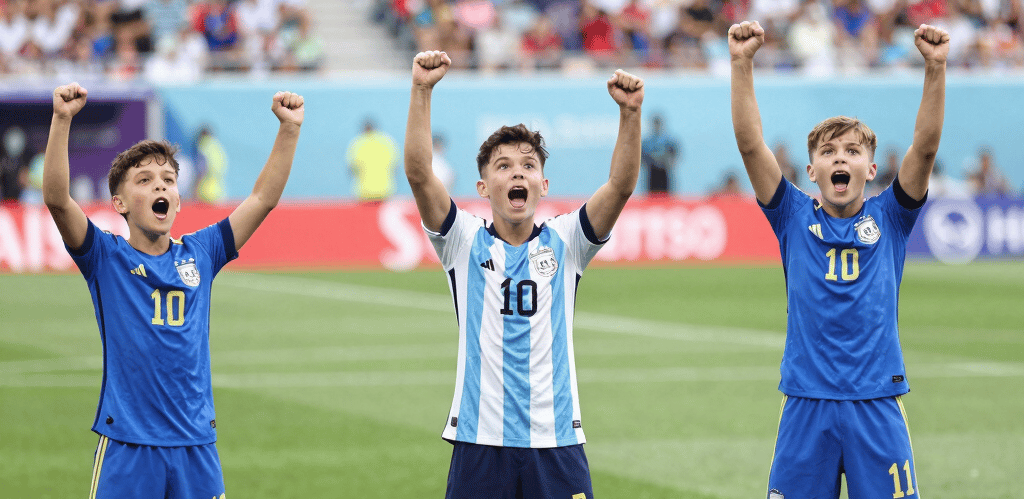 Children happily playing soccer on a sunny field with a coach guiding them.