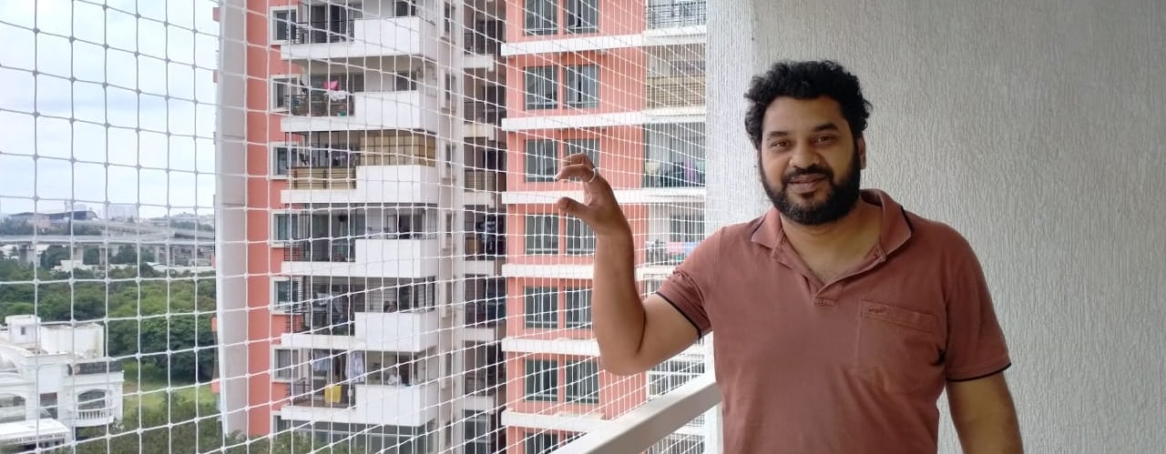 A technician carefully installing a balcony safety net on a high-rise apartment in Mumbai during a s