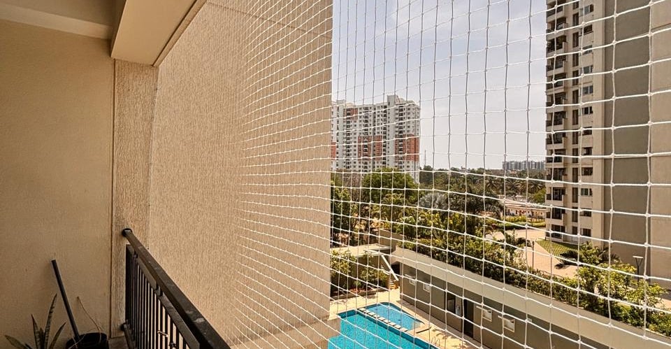A close-up of a freshly installed balcony pigeon safety net against a sunny Mumbai skyline.