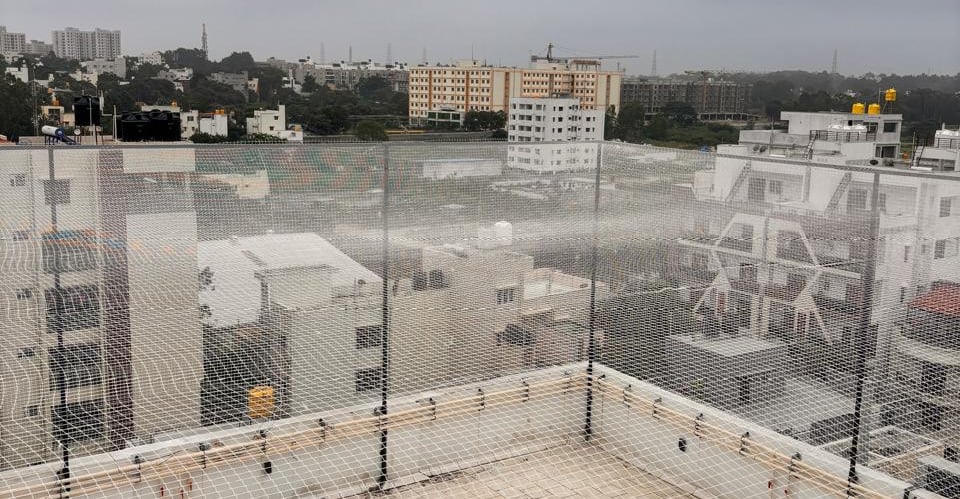 A technician carefully installing a sturdy sports net on a Mumbai terrace under bright daylight.