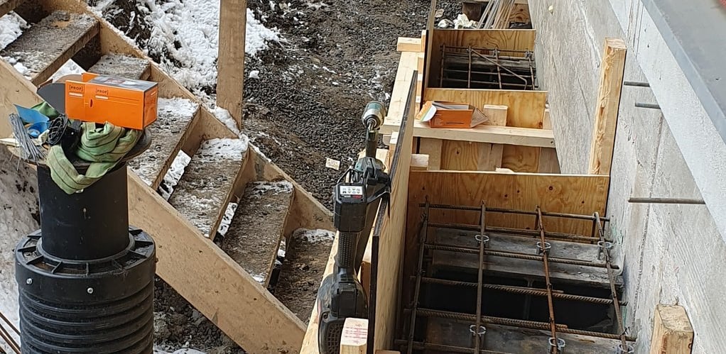 Concrete foundation formwork and rebar installation at a winter construction site next to a building.