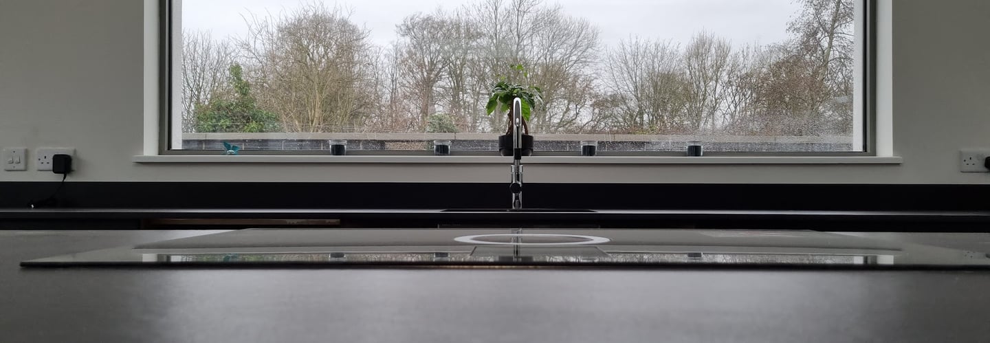 Modern kitchen sink with a chrome faucet in front of a large picture window overlooking a winter forest.