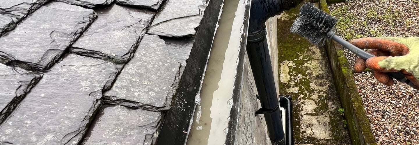 a person cleaning a roof gutter with a brush