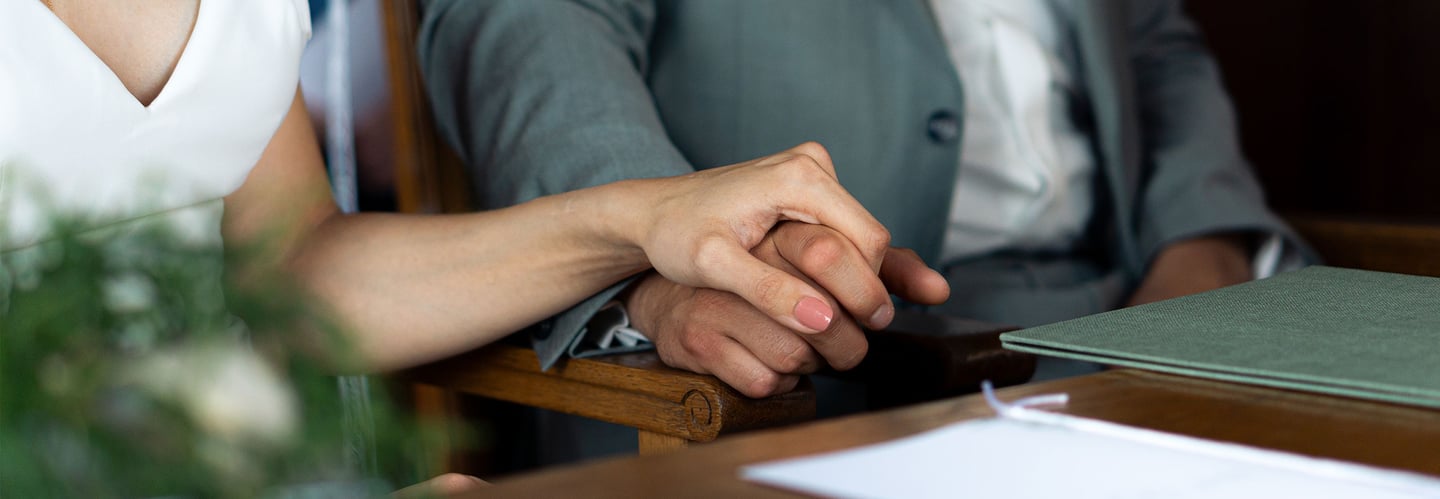 Braut und Bräutigam halten während der Trauung Hände. Emotionales Detailfoto von Just Perspectives.