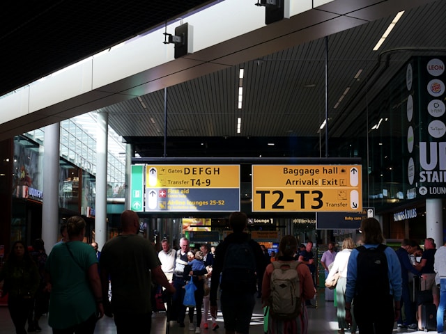 Crowd of travelers walking through a busy airport terminal past directional signs for gates and baggage.