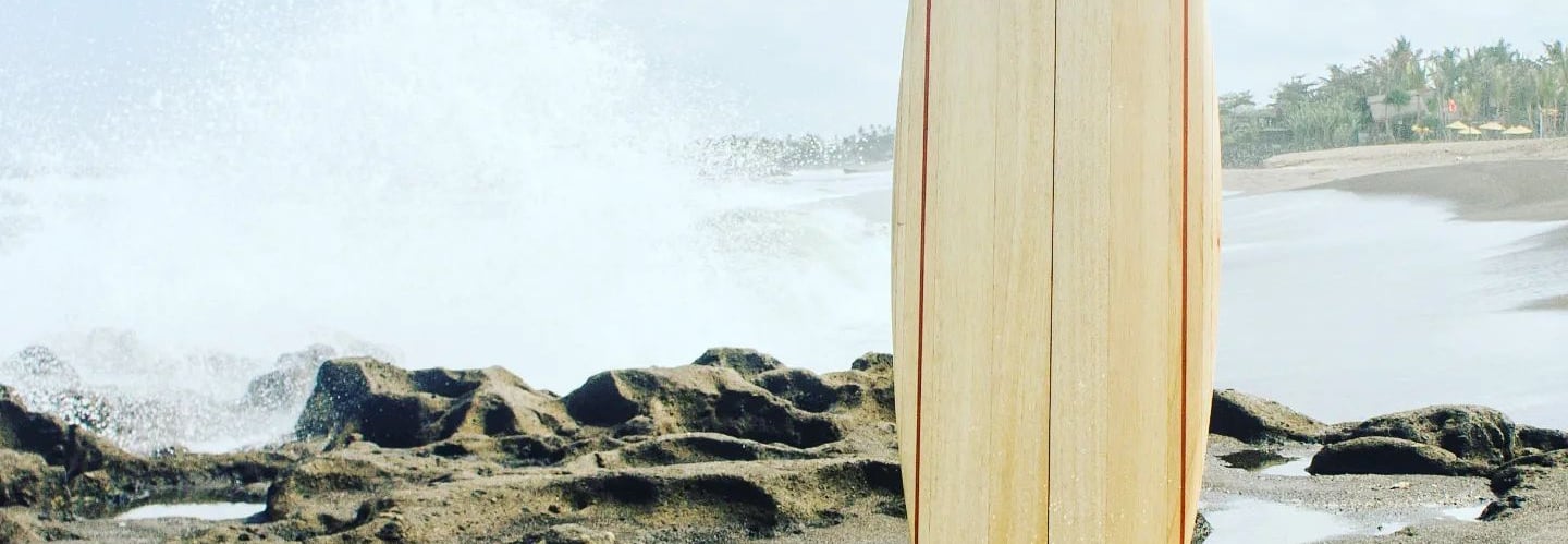 Handmade balsa surfboard standing on coastal rocks