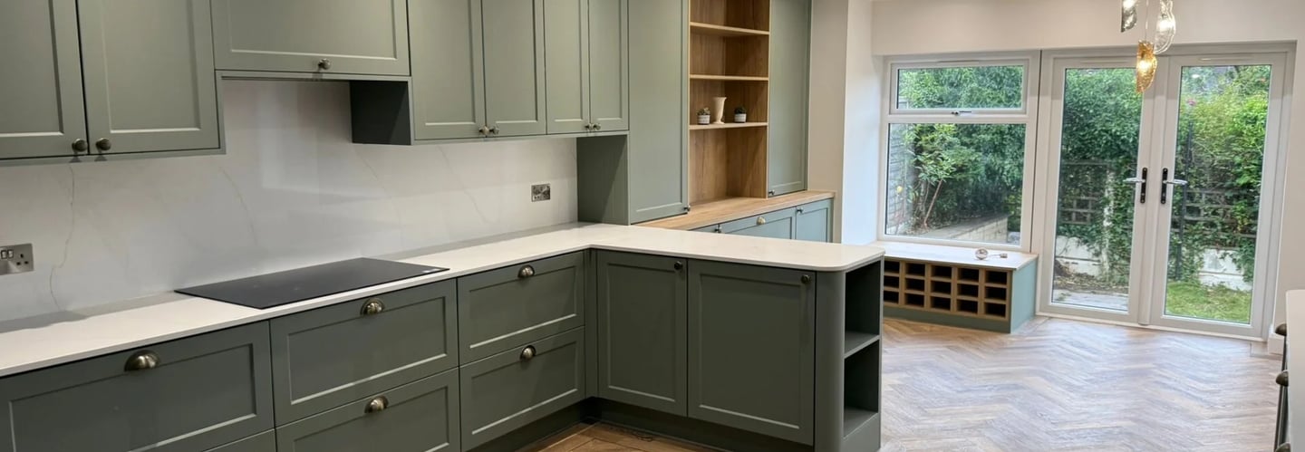 Modern sage green shaker kitchen cabinets with white marble countertops and oak herringbone flooring.