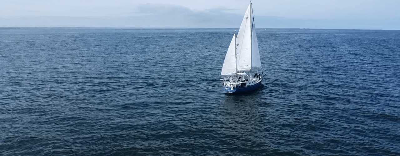 Sailing vessel Our Passion with three sails up heading towards the horizon