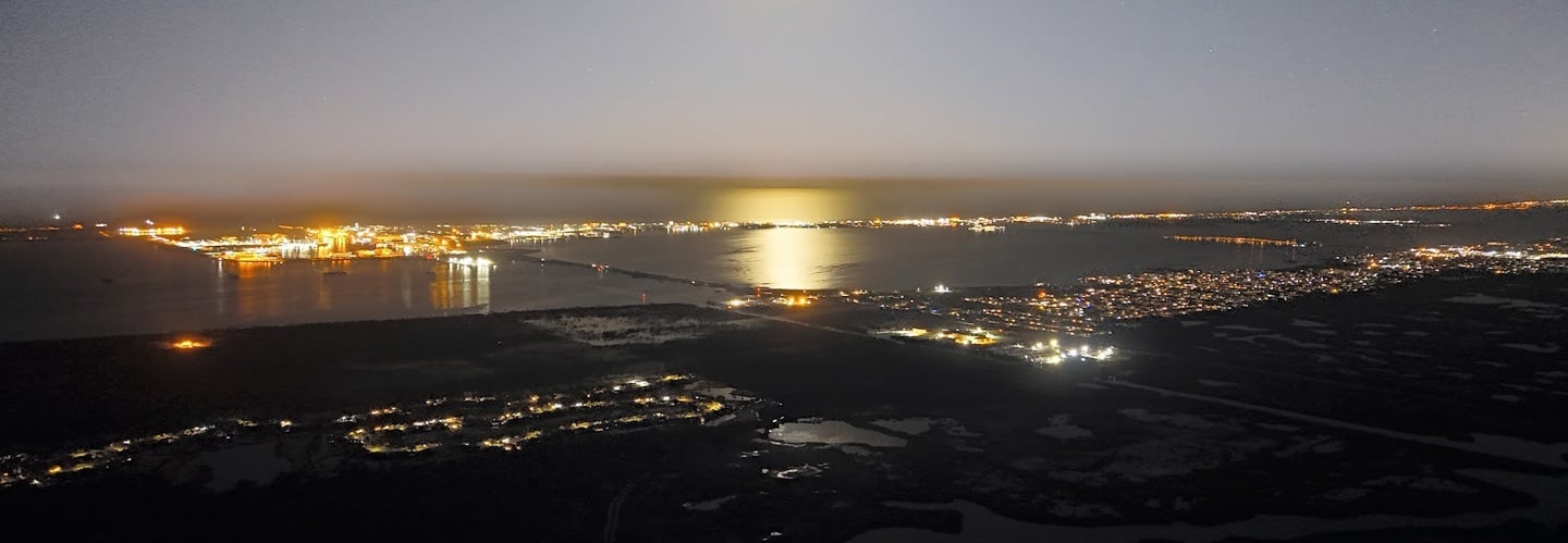A stunning nighttime aerial view of a coastal cityscape illuminated by lights from buildings.