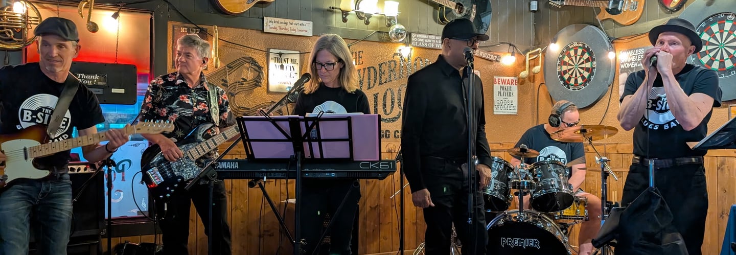 BSide blues performing classic rock music on a small stage inside a rustic bar.