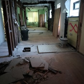 Interior home demolition showing exposed wall studs, debris, and gutted bathroom renovation.