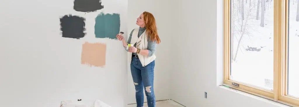 Kobieta stoi przed ścianą i porównuje próbki farb