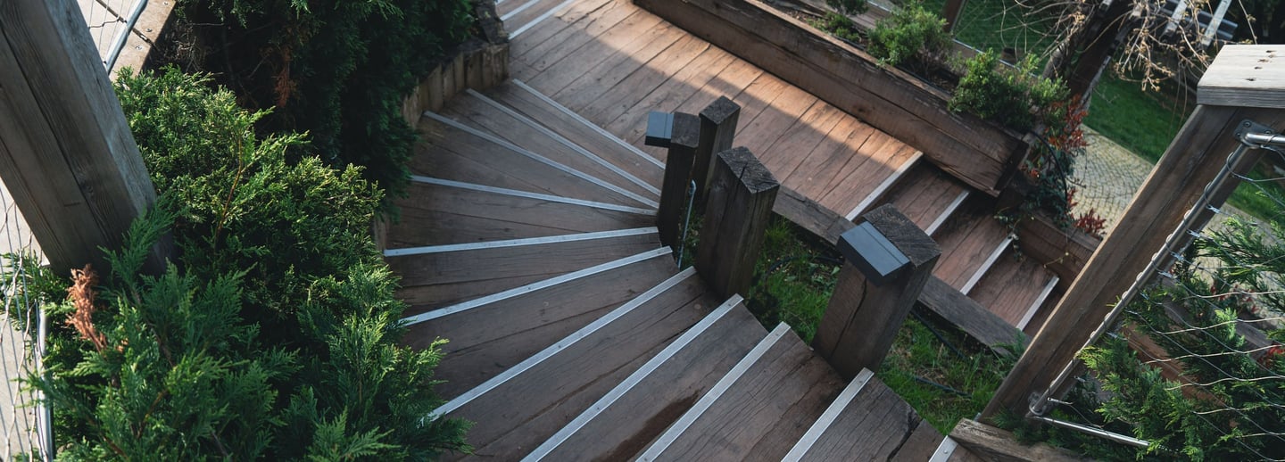 Winding wooden outdoor staircase with metal non-slip stair treads and green landscaping.