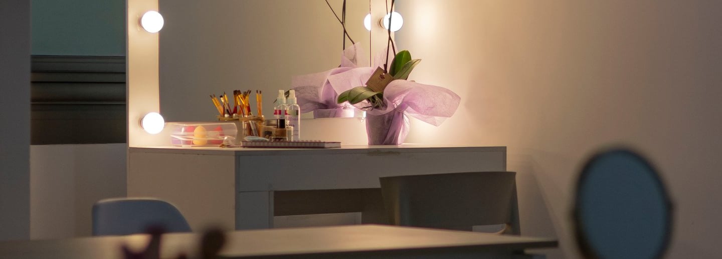 Tocador de maquillaje profesional con espejo Hollywood iluminado, planta de orquídea y herramientas 