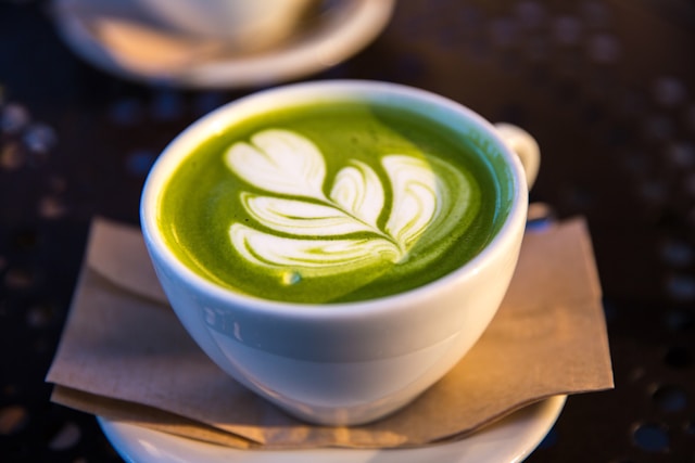 A white cup of green matcha tea latte with a leaf-shaped foam art design