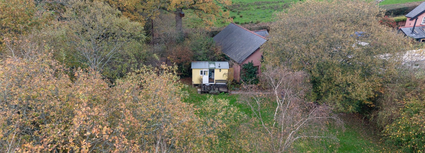 Aerial view of a yellow shepherd hut tucked into an autumn forest near a green meadow.