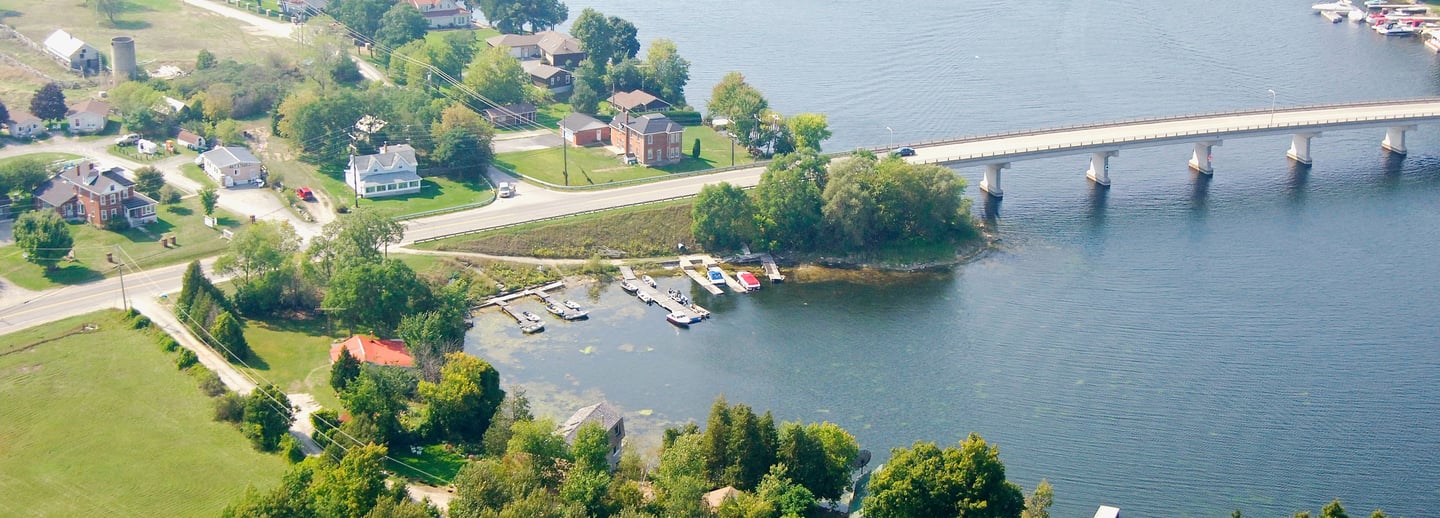 Aerial view of a scenic river with a concrete bridge, waterfront homes, and private boat docks.