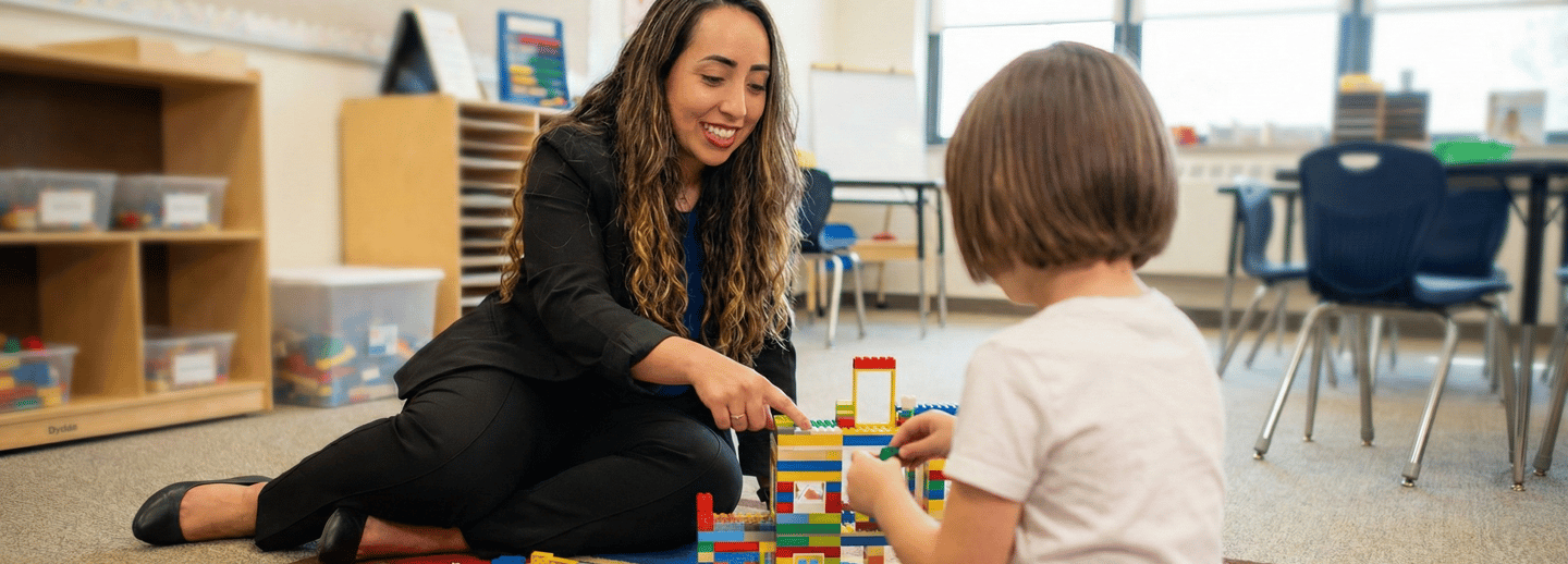Julie Granata sorri enquanto realiza atividade lúdica com blocos de montar com uma criança em ambiente acolhedor