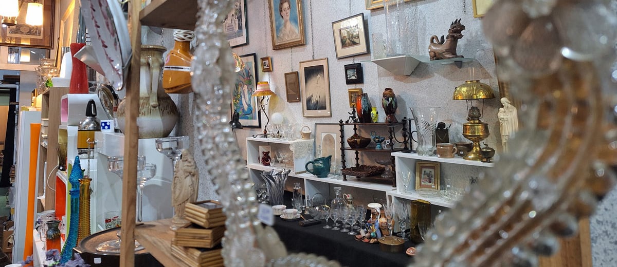 Dans le reflet d'un miroir vénitien, on voit bibelots, lampes, tableaux, verrerie ancienne.