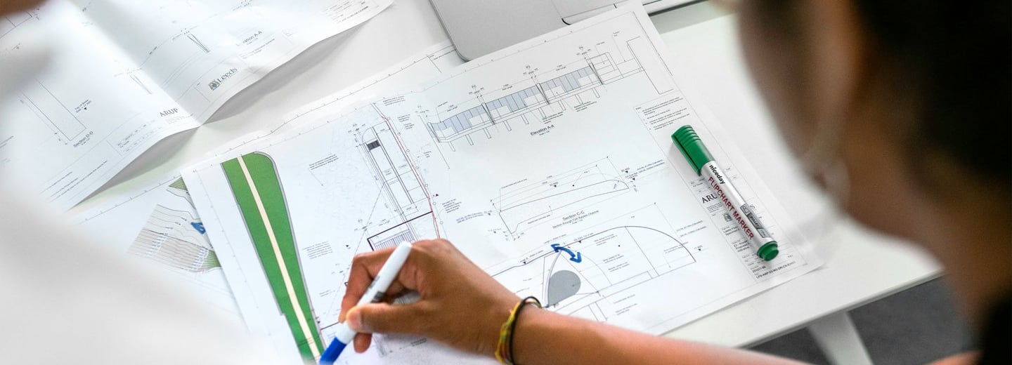 Two architects reviewing landscaping blueprints and site plans on a desk with a laptop.