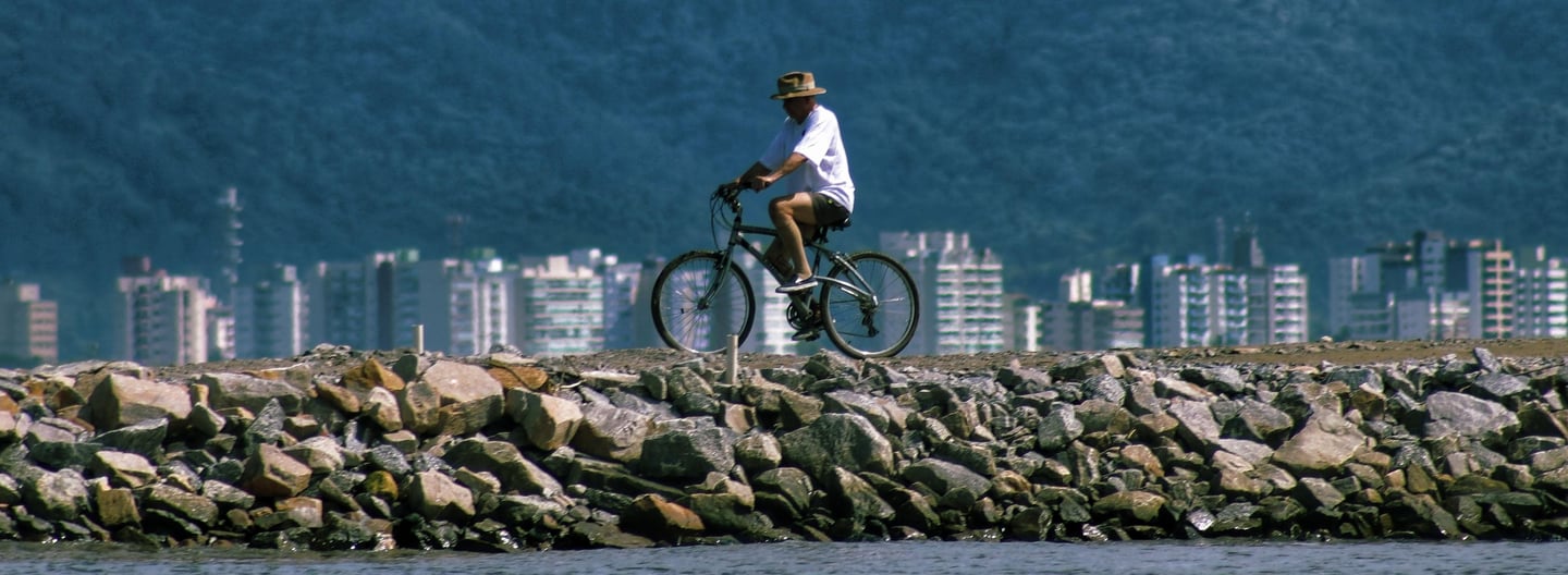 Homem andando sobre enroncamento do rio juqueriquerê com prédios do centro de caraguá ao fundo