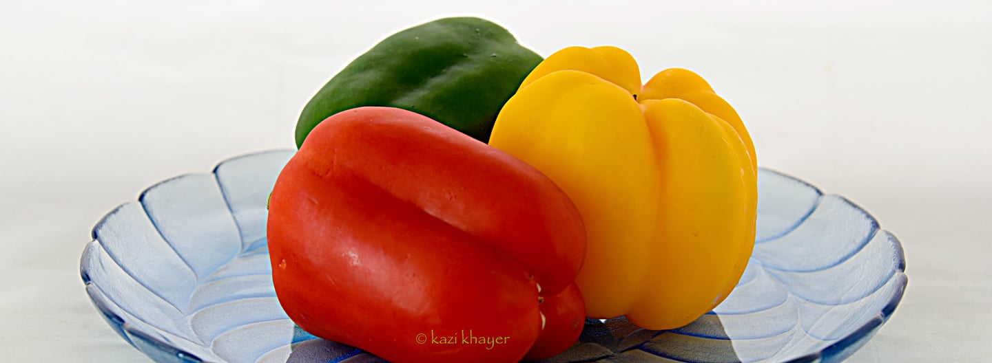 Picture of bell pepper—green red and yellow—placed on a glass plate.