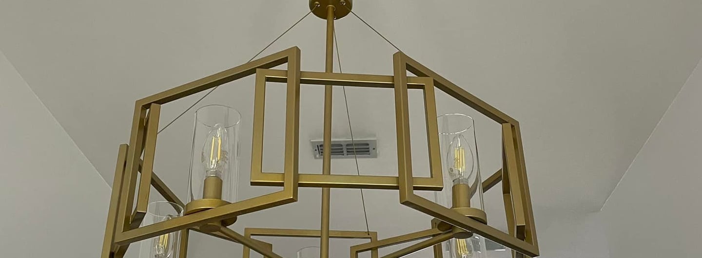 Modern gold geometric chandelier with Edison bulbs hanging from an ornate white ceiling medallion.