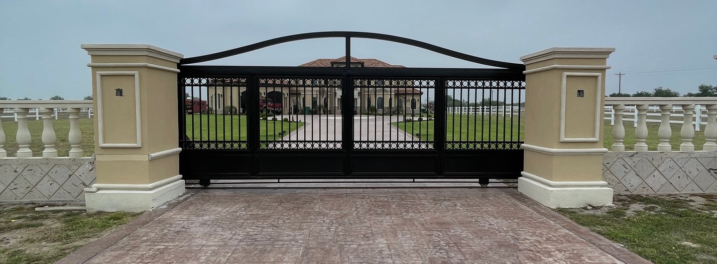 Automatic black wrought iron driveway gate with stone pillars leading to a luxury estate.