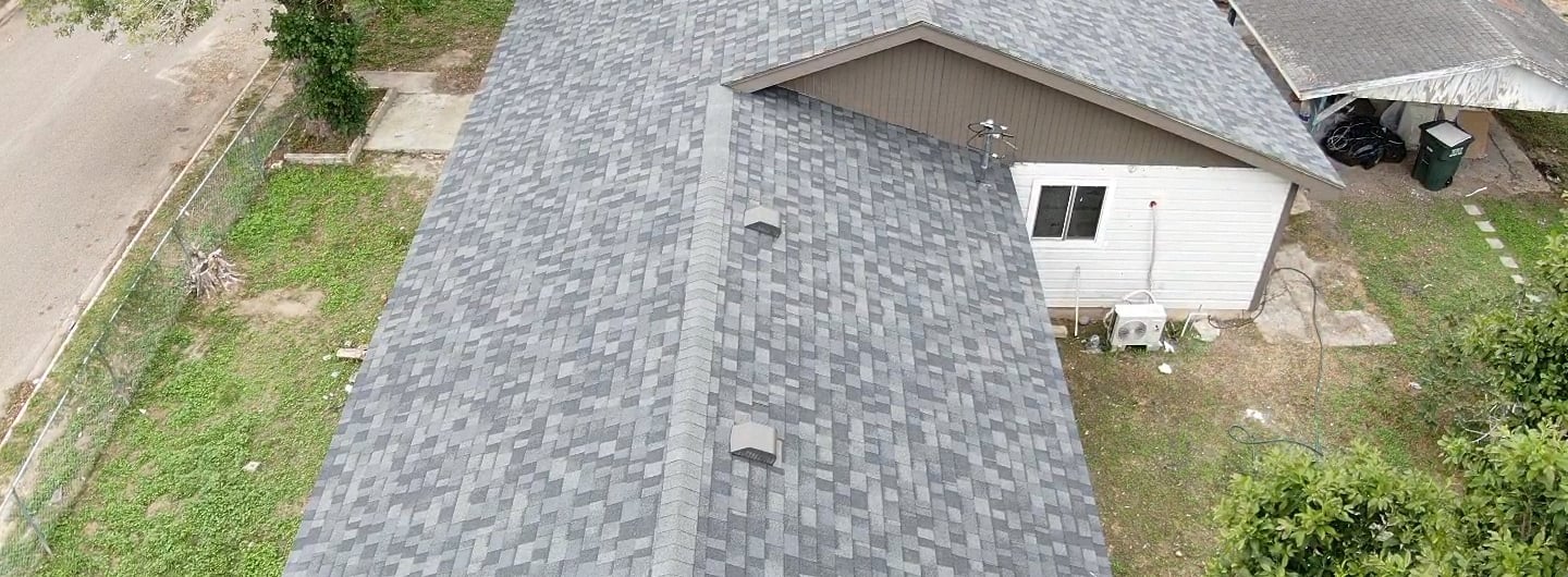 Aerial view of a residential house featuring newly installed gray architectural asphalt roof shingles.