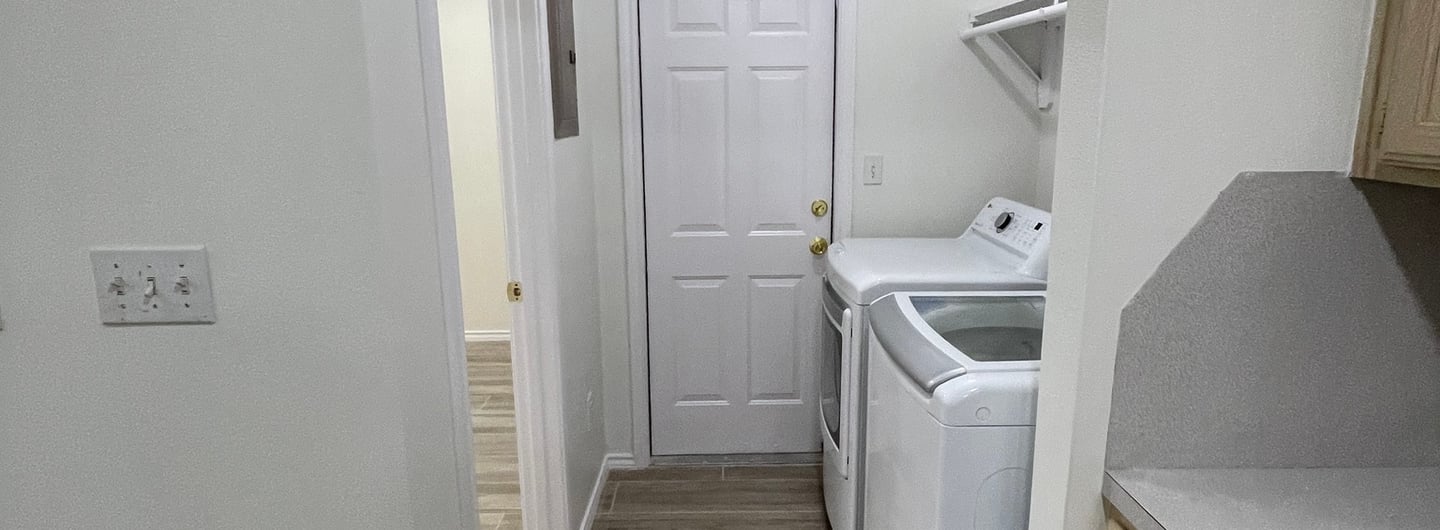 A small laundry room with white washer and dryer, wood cabinets, and gray wood-look tile flooring.