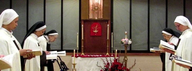 Carmelite nuns praying in the choir with the Blessed Sacrament exposed in the background.