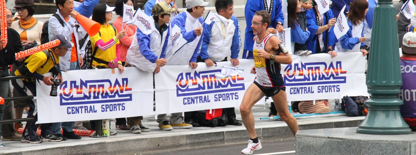 Coach Scott Brown running the Osaka marathon with a crowd of people cheering him on.