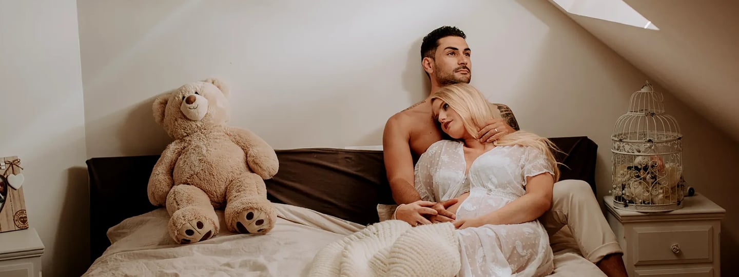 une femme enceinte pose dans son lit avec son conjoint pour une séance photo grossesse
