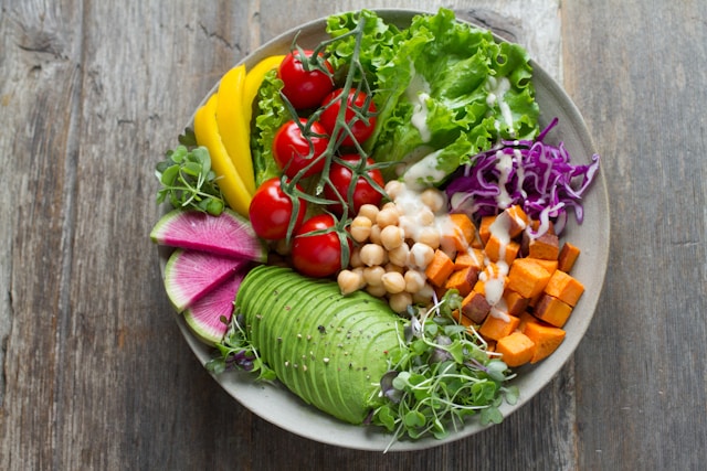 A vibrant vegan Buddha bowl with sliced avocado, sweet potato, chickpeas, and fresh vegetables on a wooden table.