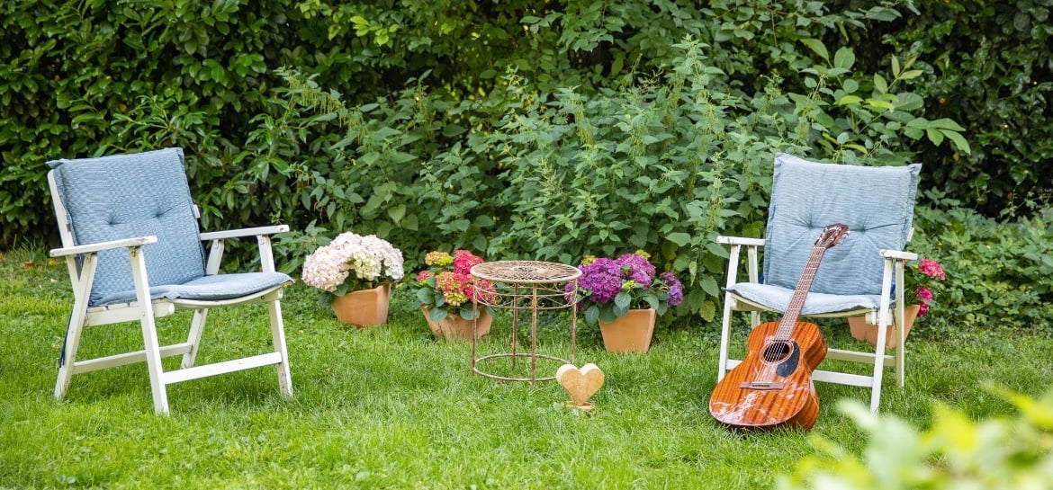 Zwei Stühle im Garten, eine Gitarre lehnt am Stuhl Blumen im Hintergrund