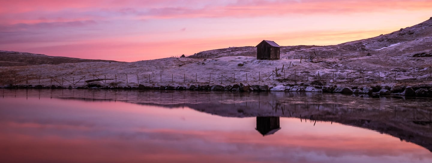 Lake near Nes on Eysturoy reflecting sunset sky and surrounding hills, calm and minimalist Faroe Islands landscape