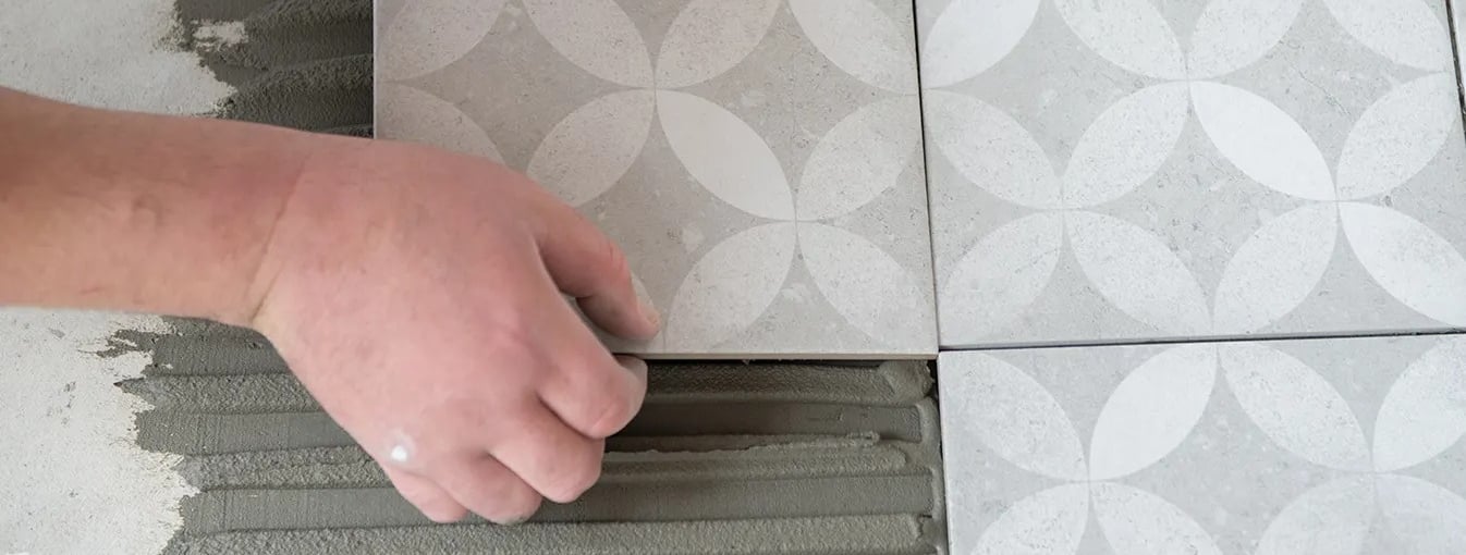 Zbliżenie na płytki, które układa pracownik. Płytki są układane bez fug