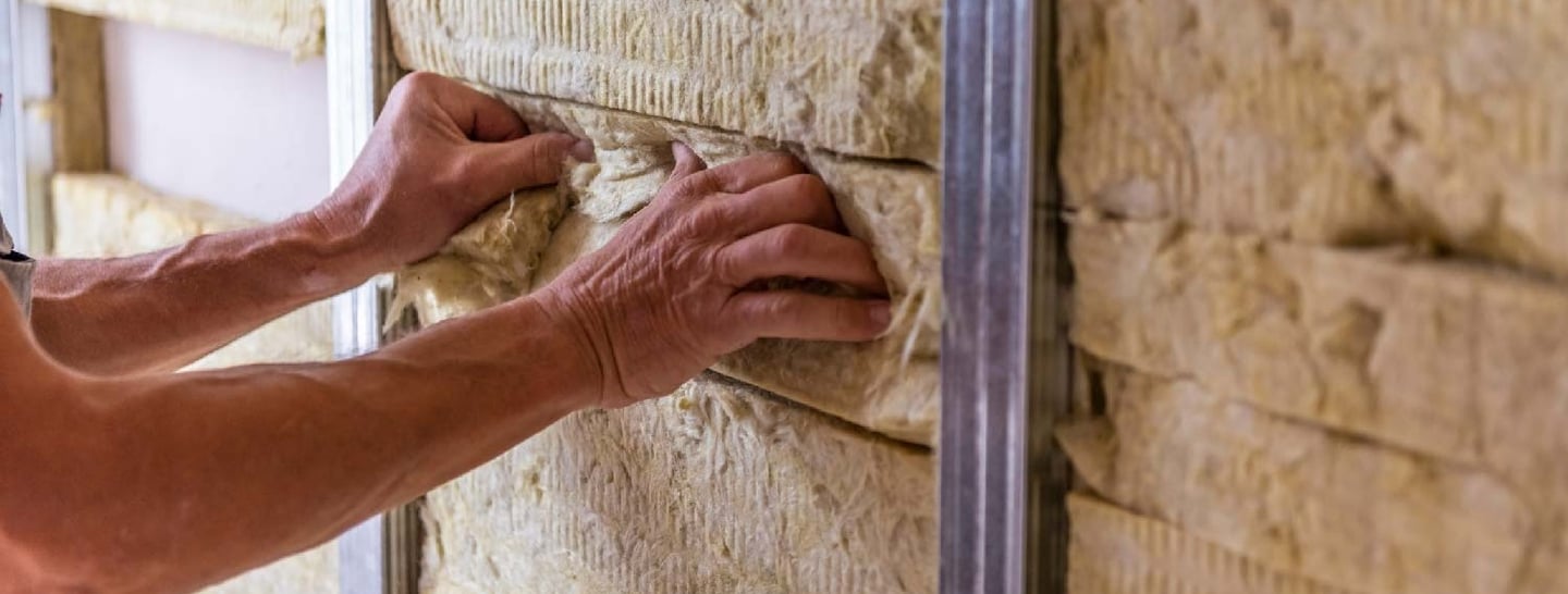 Pracownik układa wełnę mineralną między elementy stelaża aluminiowego ścianki k-g