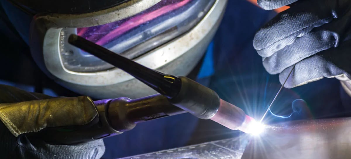a person welding a piece of metal with a torch in the background