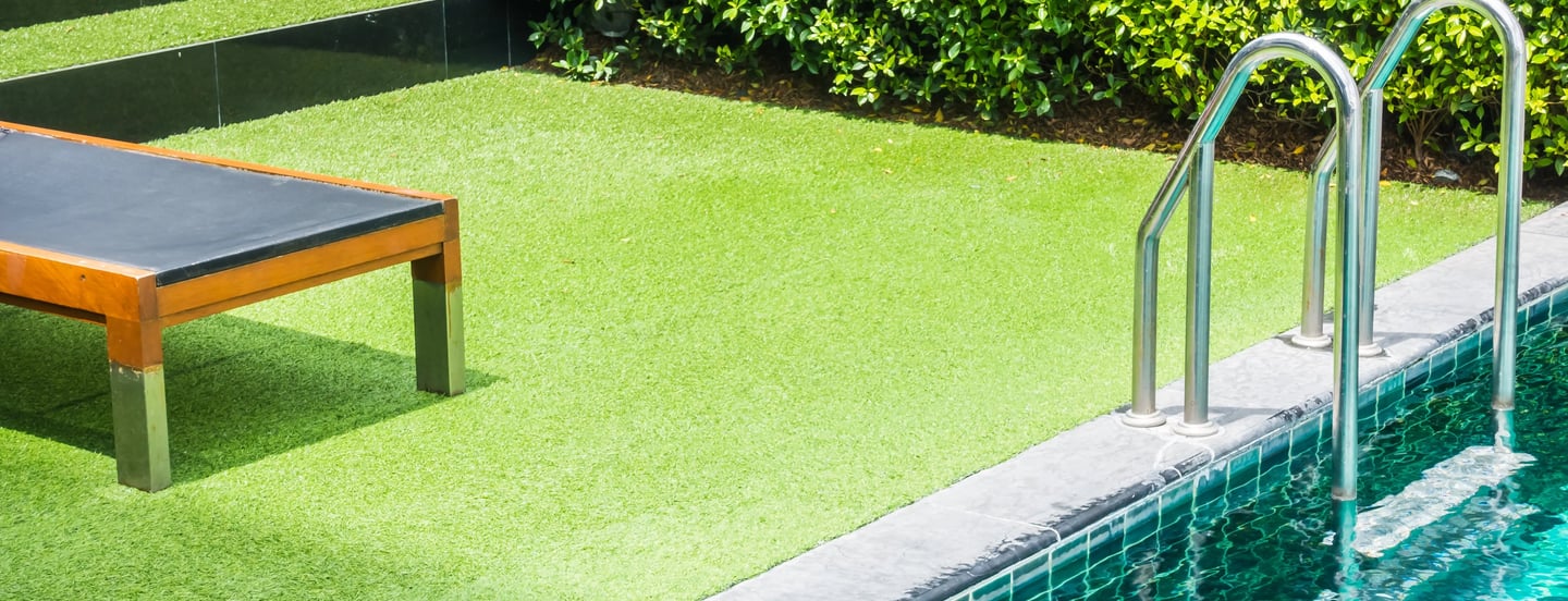 Luxury swimming pool with artificial grass turf, a wooden sun lounger, and stainless steel handrails.