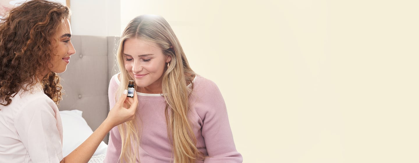 A woman holds an PurAroma essential oil bottle for another woman to smell.