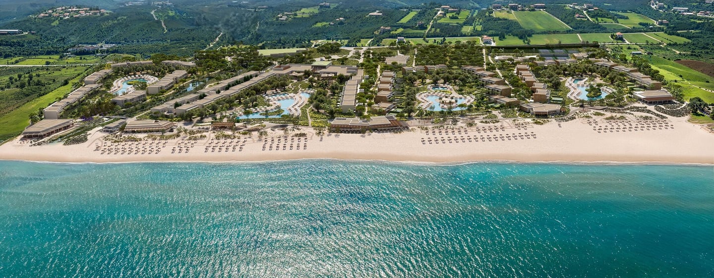 Aerial view of Ikos Kissamos resort with turquoise ocean water, sandy beach, and mountain backdrop.
