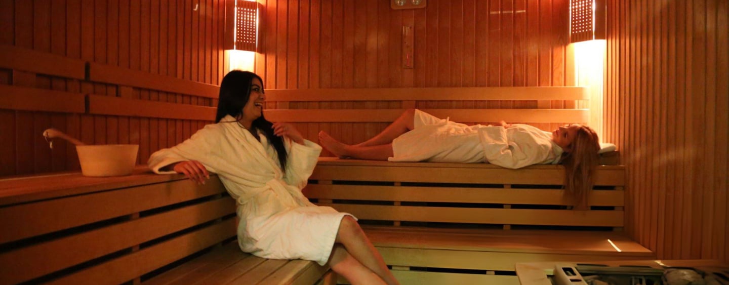 Two women in white robes relaxing and talking inside a warm, wooden luxury massage in hurghada