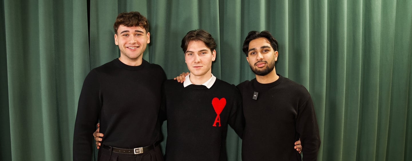 three men standing next to each other in front of a curtain