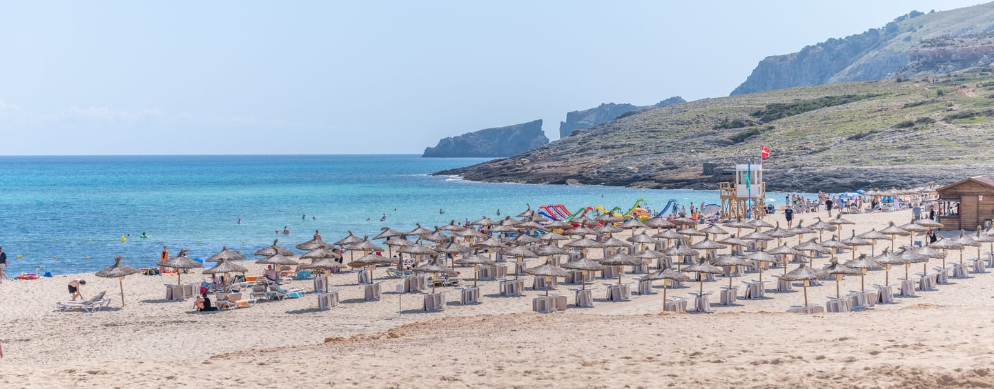 Cala Mesquida beach with sunbeds and people swiming in the sea