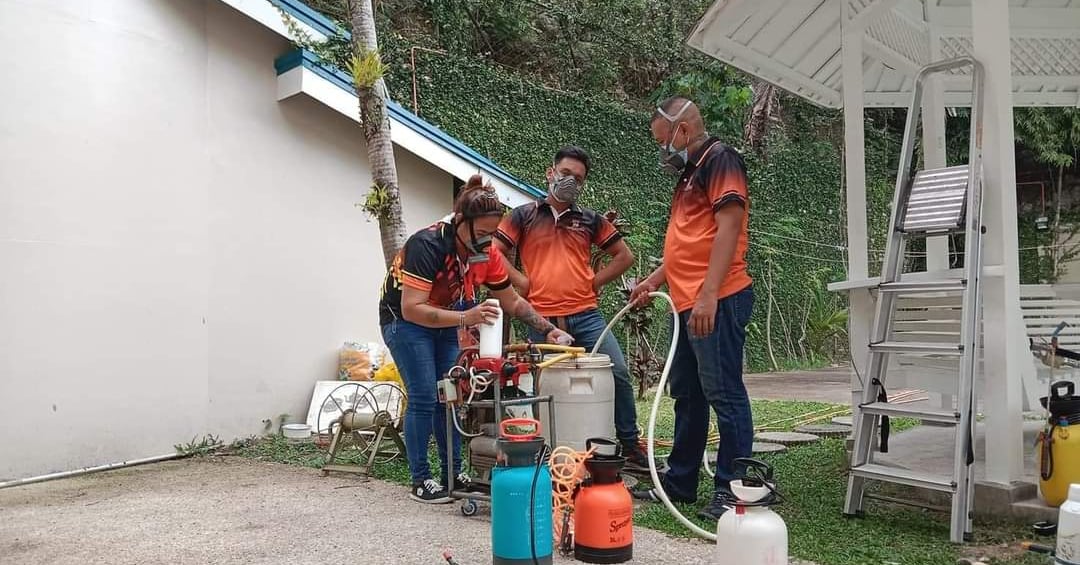 Jansen pest control team in orange uniforms preparing disinfection equipment and sprayers outdoors.