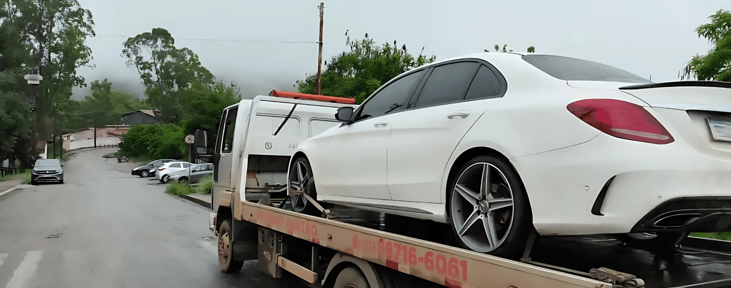 Guincho da Agatão transportando carro de luxo branco em rua úmida e arborizada de Ouro Preto.