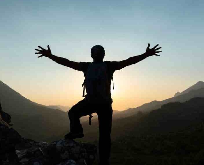 silhouette of person on top of a mountain arms outstretched