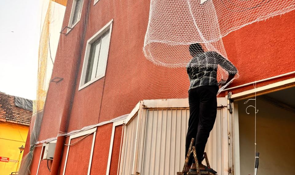A friendly technician installing a safety net on a Mumbai construction site under a clear blue sky.